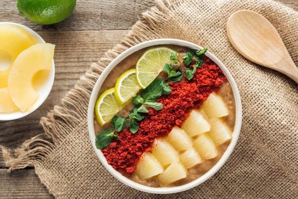 Top view of fresh smoothie bowl with lemons, mint and pineapples on sackcloth with ingredients — Stock Photo