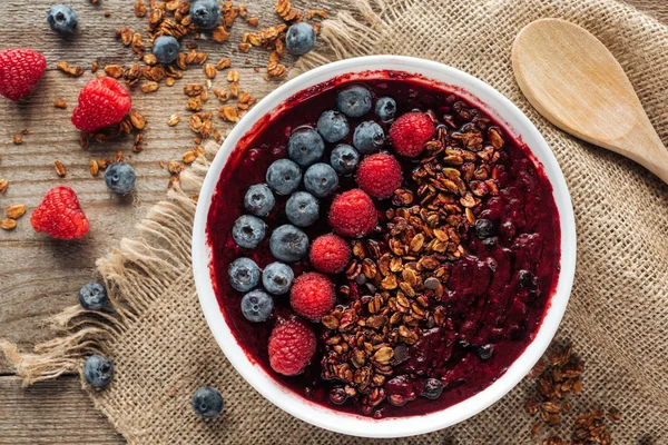 Vista dall'alto di deliziosa ciotola di frullato biologico con bacche e muesli su sacco — Foto stock