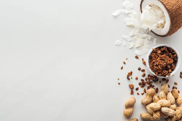 Vista superior de granola, cacahuetes y coco con hojuelas sobre fondo blanco con espacio para copiar - foto de stock