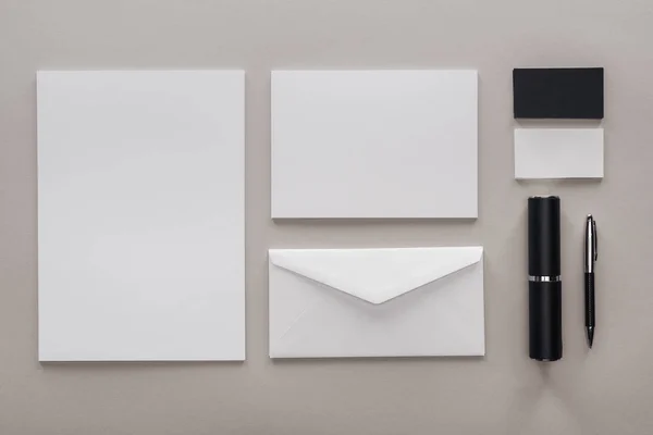 Flat lay with blank white papers, envelope and stationery on grey background — Stock Photo