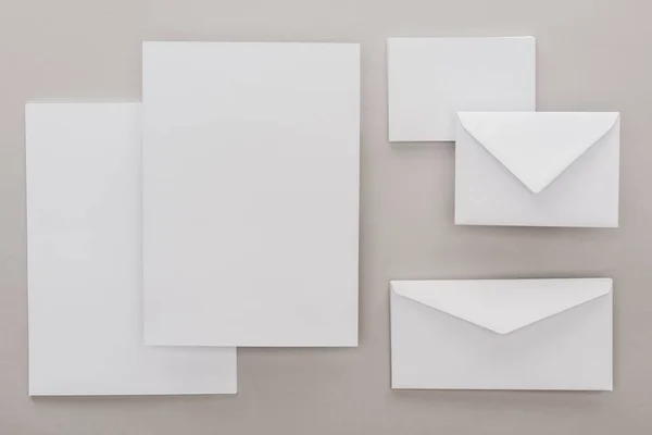 Flat lay with white blank papers and envelopes on grey background — Stock Photo