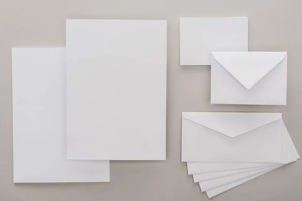 Vista superior de papeles blancos vacíos y sobres sobre fondo gris - foto de stock