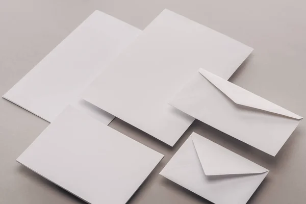 Flat lay with empty white papers and envelopes on grey background — Stock Photo