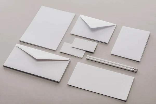 Pose plate avec enveloppes, cartes, feuilles de papier et crayons sur fond gris — Photo de stock