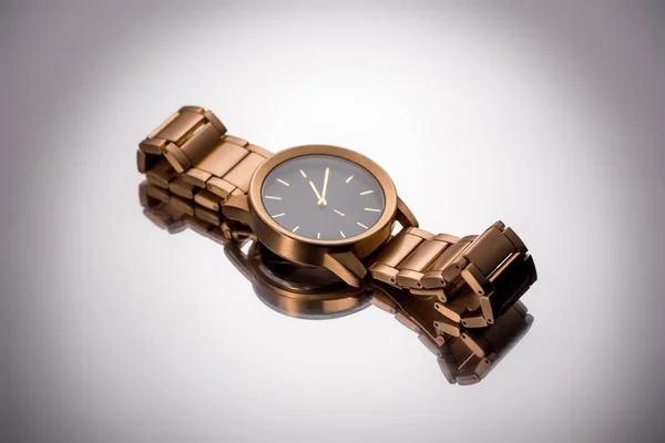 Goldene Armbanduhr auf Glasoberfläche auf weißem Hintergrund liegend — Stockfoto
