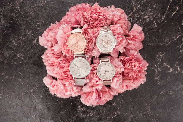 Top view of elegant wristwatches lying on blooming pink flowers on grey surface — Stock Photo