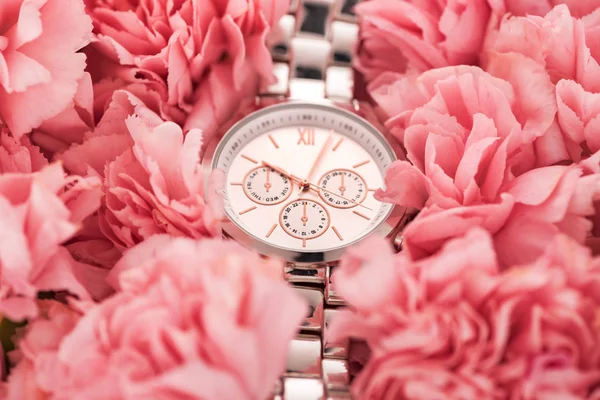 Elegant wristwatch lying on blooming pink carnations — Stock Photo