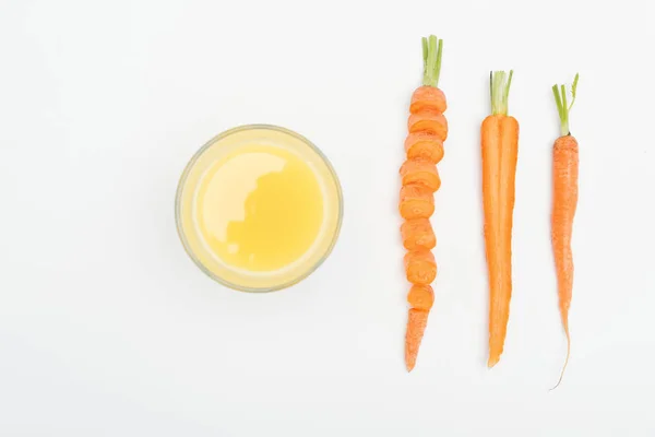 Draufsicht auf Schüssel mit frischem Karottensaft, in Scheiben geschnittenen Möhren, geschnittenen und ganzen Möhren isoliert auf weiß — Stockfoto