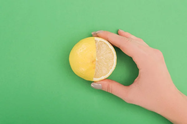Partial view of woman holding fresh partially cut lemon on green background — Stock Photo