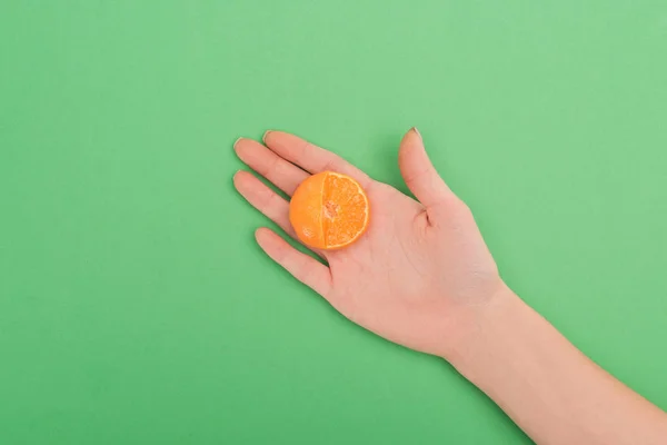 Partial view of female hand with partially cut tangerine on green background — Stock Photo