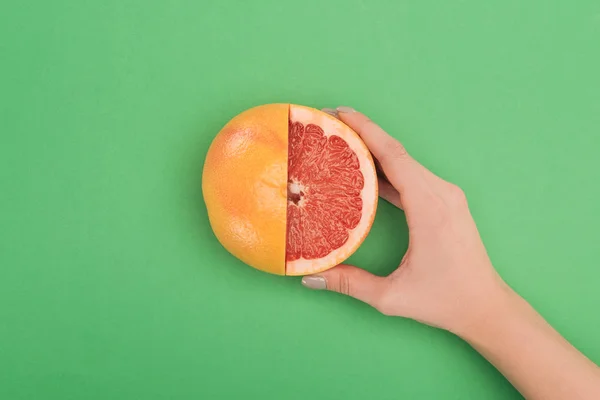 Частичный вид женской руки со свежим частично разрезанным грейпфрутом на зеленом фоне — стоковое фото