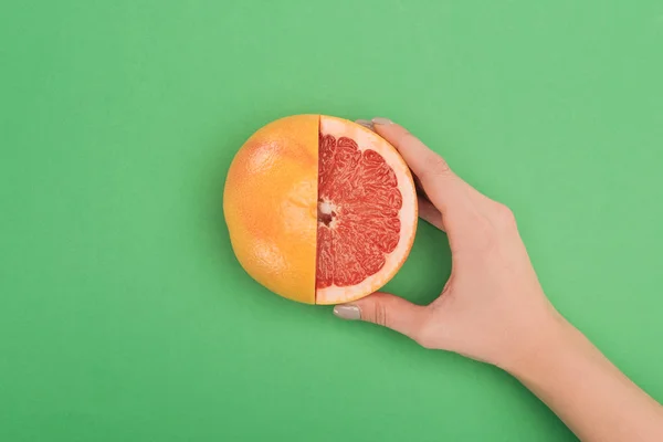 Vista parcial de la mano femenina con pomelo fresco parcialmente cortado sobre fondo verde - foto de stock