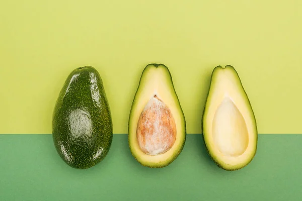 Draufsicht auf ganze Avocado- und Avocadohälften auf zweifarbigem Hintergrund — Stockfoto