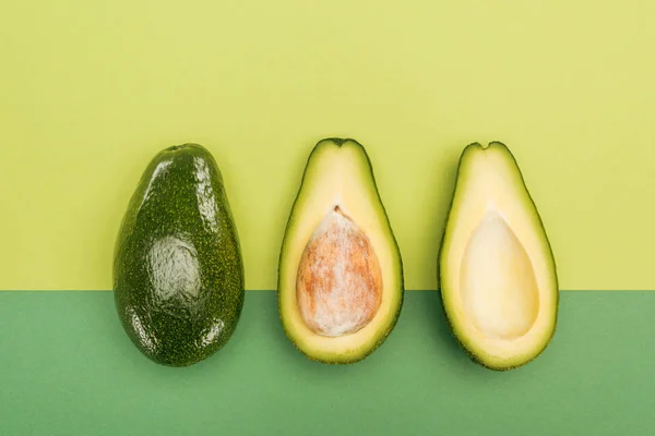 Top view of whole avocado and avocado halves on bicolor background — Stock Photo