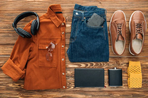 Flat lay com fones de ouvido, frasco de quadril e roupas em fundo de madeira — Fotografia de Stock