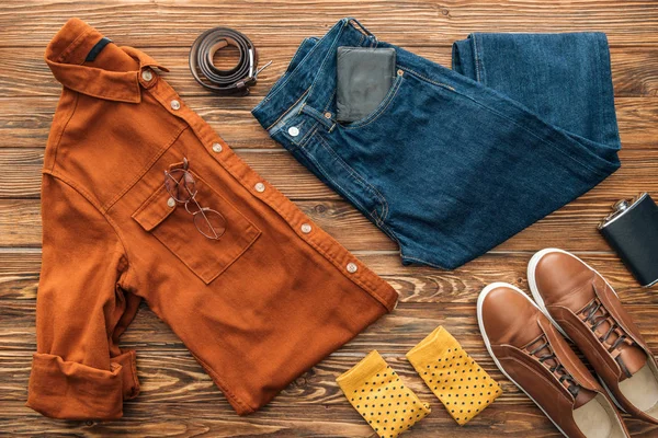 Puesta plana con camisa, jeans y zapatos con accesorios sobre fondo de madera - foto de stock