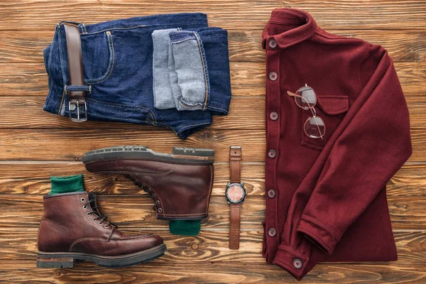 Flat lay with leather boots, jeans and shirt on wooden background — Stock Photo