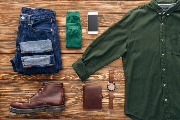 Puesta plana con jeans, camisa verde y smartphone sobre fondo de madera - foto de stock