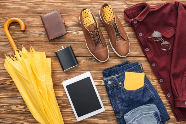 Flat lay with male clothes, digital tablet and yellow umbrella on wooden background — Stock Photo