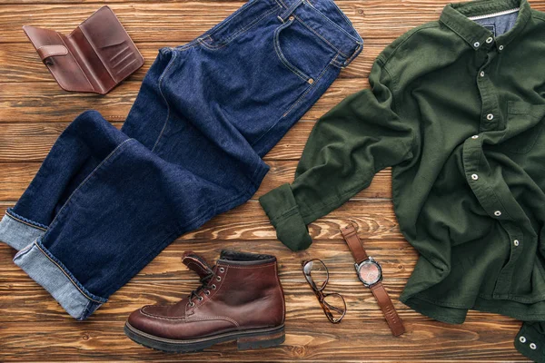 Vista superior de camisa verde, jeans y billetera de cuero sobre fondo de madera - foto de stock