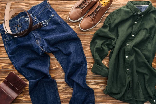 Вид сверху зеленой рубашки, обуви и джинсов на деревянном фоне — стоковое фото