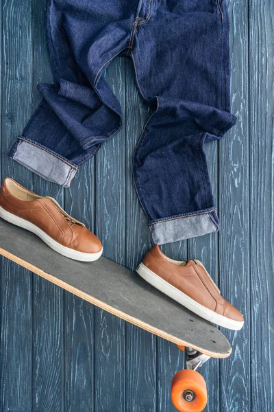 Top view of jeans, shoes and longboard on wooden background — Stock Photo