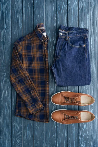 Top view of checkered shirt, jeans and brown shoes on wooden background — Stock Photo