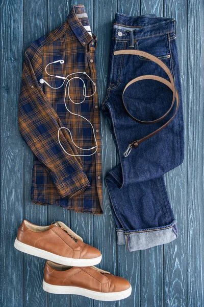 Vista superior de jeans, camisa a cuadros y auriculares sobre fondo de madera - foto de stock