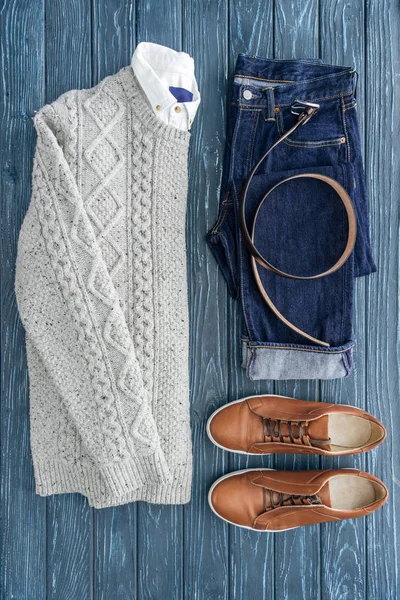 Puesta plana con suéter de punto, jeans y zapatos marrones sobre fondo de madera - foto de stock