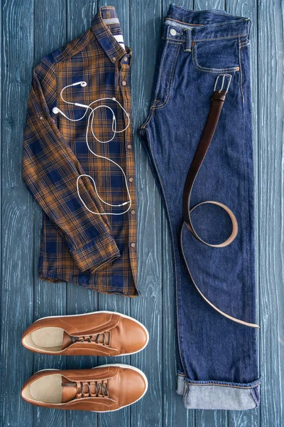 Vue de dessus des vêtements, chaussures et écouteurs masculins sur fond en bois — Photo de stock
