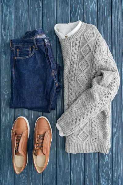 Flache Lage aus grauem Strickpullover, Jeans und Schuhen auf hölzernem Hintergrund — Stockfoto
