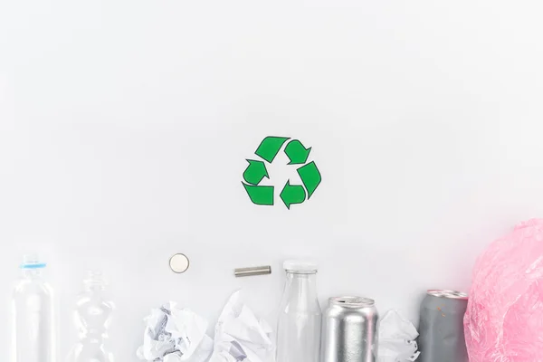 Top view of cans, plastic and glass bottles, batteries, paper, recycling sign and pink plastic bag — Stock Photo