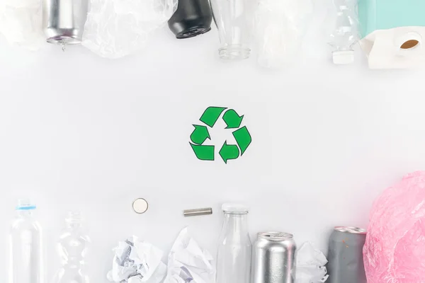 Draufsicht auf Dosen, Plastik- und Glasflaschen, Batterien, Papier, Recyclingschild, Kartonflasche und rosa Plastiktüte — Stockfoto