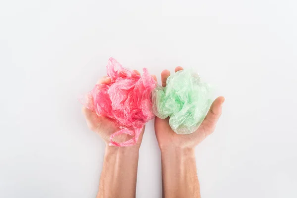 Cropped view of man holding pink and green plastic bags on grey background — Stock Photo