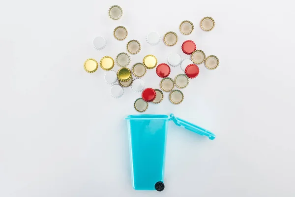 Top view of bottle caps falling down into blue toy trashcan on grey background — Stock Photo