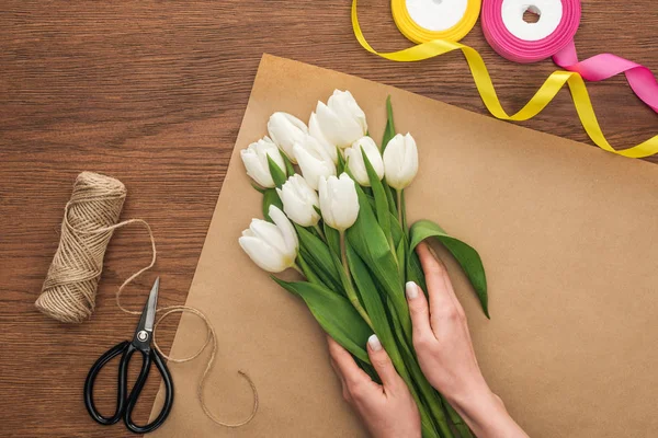 Vista ritagliata su fiorista facendo mazzo di tulipani bianchi su sfondo di legno — Foto stock