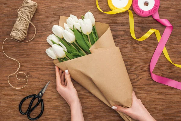 Vista ritagliata su fiorista femminile rendendo bouquet primavera con mestiere di taglio su sfondo di legno — Foto stock