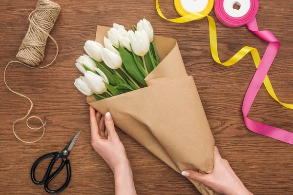 Vista recortada de en floristería femenina haciendo ramo de primavera con artesanía de corte sobre fondo de madera - foto de stock