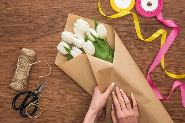 Vista ritagliata su fiorista rendendo bouquet tulipano con mestiere di taglio su sfondo di legno — Foto stock
