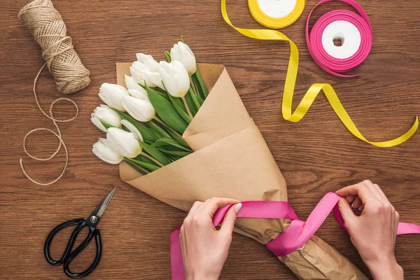 Vue recadrée de sur fleuriste faisant bouquet de fleurs de tulipes de printemps avec ruban sur fond en bois — Photo de stock
