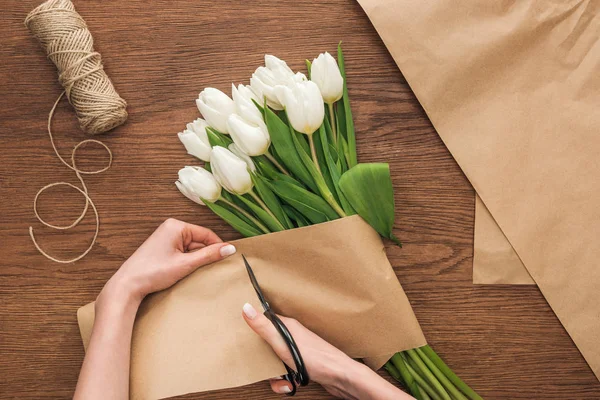 Vue partielle de sur fleuriste couper du papier artisanal tout en faisant bouquet de printemps sur fond en bois — Photo de stock