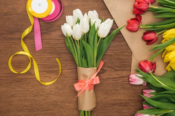 Ansicht von Frühlingsstrauß, Tulpen, Bändern und Bastelpapier auf Holzgrund — Stockfoto