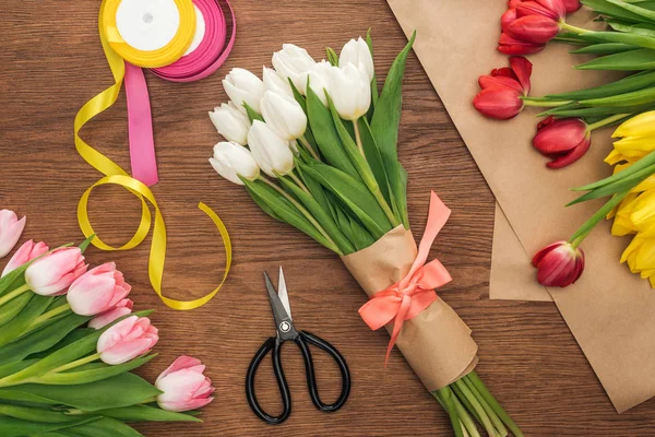 Vue de dessus du bouquet de floristique, des tulipes, des rubans et du papier d'artisanat sur fond en bois — Photo de stock
