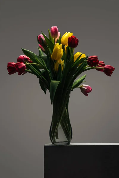 Buquê de tulipas coloridas em vaso de vidro em cinza — Fotografia de Stock