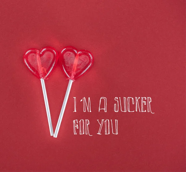 Two heart shaped lollipops on red background with 