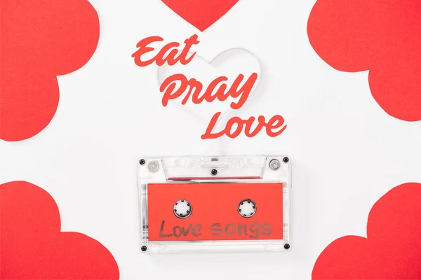Draufsicht auf Audiokassette mit 'Liebeslieder' -Schriftzug und herzförmigen Karten isoliert auf weißem, Valentinstag-Konzept mit 