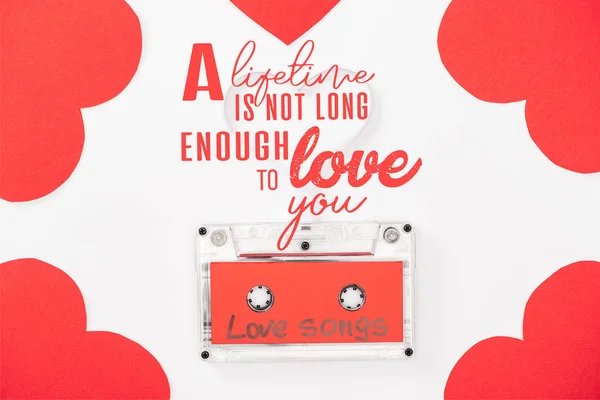Vista superior de cassette de audio con letras de 'canciones de amor' y tarjetas en forma de corazón aisladas en blanco, San Valentín concepto de día con 