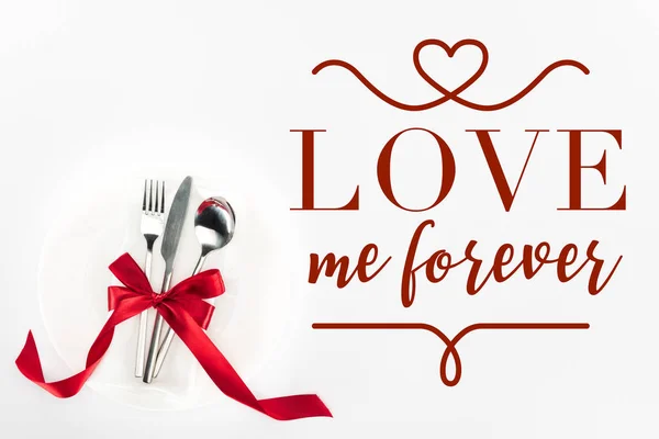 Vista elevata di forchetta, coltello e cucchiaio avvolti da fiocco festivo rosso su piatto isolato su bianco, concetto San Valentino con scritta 