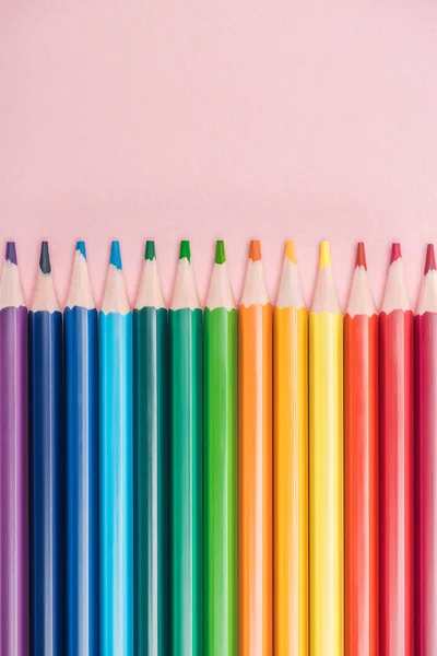 Crayons multicolores arc-en-ciel disposés en ligne horizontale sur fond rose, concept lgbt — Stock Photo