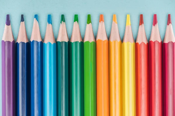 Vue de dessus des crayons multicolores arc-en-ciel disposés en ligne horizontale sur fond bleu, concept lgbt — Stock Photo